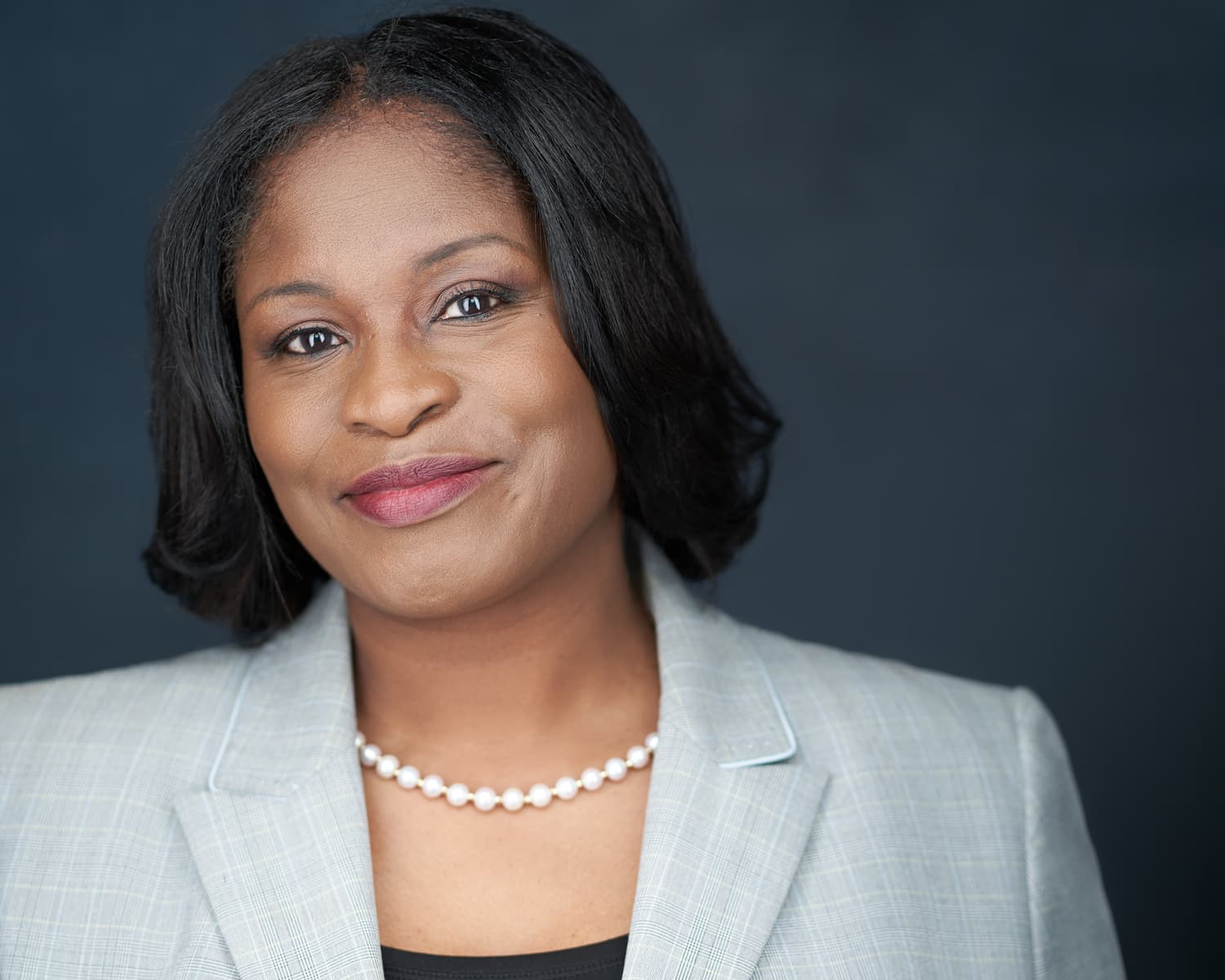 Professional corporate headshot of executive with pearl necklace and light grey blazer